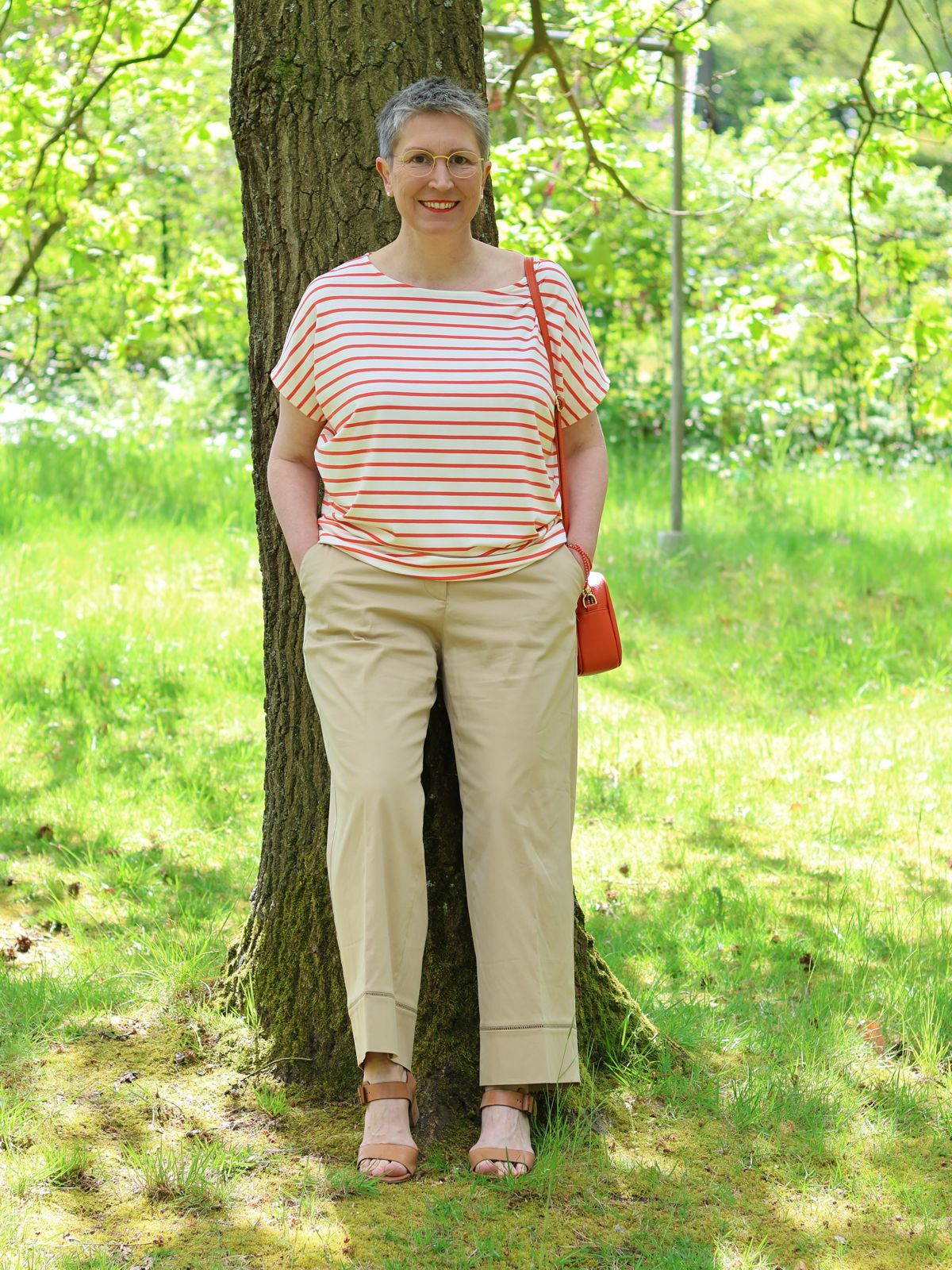 Ines Meyrose - Outfit 2024 - Ringelshirt in orange-cremeweiß - weite Sommerhose sandfarben/beige - cognacfarbene Sandaletten mit Blocksatz - kleine Handtasche in Papaya - Korallenkette als Armband